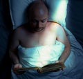 Man reading a book in bed in a ray of bright moonlight