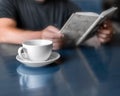 A man reading book and drinking coffee sitting in cafe or at home in kitchen at morning time. A coffee cup on dark blue table. A p Royalty Free Stock Photo