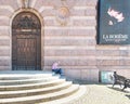 Man reading book in front of brick wall with billboard for La Boheme and door to Royal Swedish Opera House, Stockholm