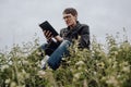 Man reading book in green hilly field. Side view of young handsome man in glasses and warm jacket reading book in open