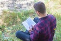 A man is reading a book in the park. Reading a book outdoors