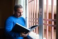 Man reading a book by the window dunring quarantine