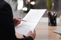 Man reading employment agreement at table in office, closeup. Signing contract