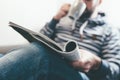 Man reading magazine or newspaper and drinking coffee while relaxing on sofa Royalty Free Stock Photo