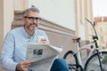 Man reading newspaper and drinking coffee in city. blurred bicycle in background Royalty Free Stock Photo