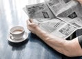 A man reading newspaper and drinking coffee sitting in cafe or at home in kitchen at morning time. A coffee cup on dark