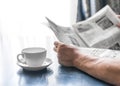 A man reading newspaper and drinking coffee sitting in cafe or at home next to kitchen window at sunny morning time. A