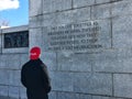 Man reading Nimitz quote on WWII Memorial wall, while wearing a `Make America Great Again` hat.