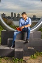 Young man sitting outdoors in New York City, reading red book Royalty Free Stock Photo