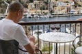 Man Reading Something on His Cellphone On a Balcony Overlooking the Symi Harbor Greece Royalty Free Stock Photo