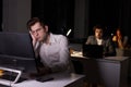 Man realising amount of work in office at night, sitting at desk working on computer