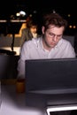 Man realising amount of work in office at night, sitting at desk working on computer