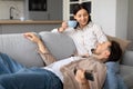 Man lying on couch with remote, woman sitting with cup, both smiling Royalty Free Stock Photo