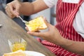 Man in red apron spreading sweet orange peel jam on toast with sun icon over table Royalty Free Stock Photo