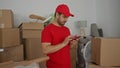 Man in red cap taps smartphone screen with finger inside building surrounded by moving boxes; efficiency Royalty Free Stock Photo