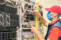 A man in a red cap works in a datacenter. A technical employee maintains computer equipment. A technician in a medical mask Royalty Free Stock Photo