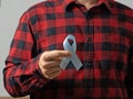 A man in a red checked shirt holds a blue ribbon with both hands-a symbol of prostate cancer awareness.