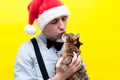 Man in red christmas santa hat, blue shirt and black suspender holding and kissing cute brown tabby cat