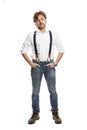 A man with red hair in a white shirt and jeans with suspenders stands. Full height. Isolated on a white background. Vertical