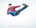 Man in red hooded sweatshirt and jeans in karate fight jump, on light background