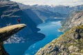 A man in a red jacket jumping on the Trolltunga rock with a blue lake 700 meters lower and interesting sky with clouds Royalty Free Stock Photo