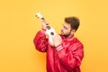 Man in a red jacket plays a Hawaiian guitar on the background of a yellow wall. Student with a beard is isolated on a yellow Royalty Free Stock Photo