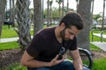 A man with a red shirt and blue jeans relaxes on a park bench playing with his aviator glasses looking down on a bright sunny day Royalty Free Stock Photo