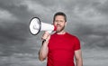 man in red shirt proclaim in loudspeaker on sky background