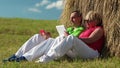 Man with red smartphone and woman with tablet computer sits near a hayrick