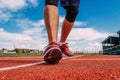 A man in red sports shoes runs on a red treadmill at the stadium in the summer, his feet are close