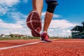 A man in red sports shoes runs on a red treadmill at the stadium in the summer, only his feet are close