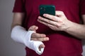 A man in a red T-shirt with a broken arm in a cast holds and uses a phone Close-up Royalty Free Stock Photo