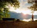 Man in red tshirt walk at lake bank. Empty wooden bench, tree stump