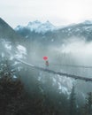 A man with a red umbrella crosses a suspension bridge in the mountains Royalty Free Stock Photo