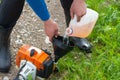 A man refuels a lawn mowers gasoline engine from a plastic tank