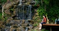 Man relaxes with cat in his arms on pier near picturesque waterfall in jungle. Relaxing in nature helps you to be alone Royalty Free Stock Photo