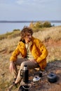 Man relaxing by campfire in forest by river sitting alone. Summer camping. Traveling concept Royalty Free Stock Photo