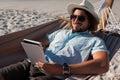 Man relaxing on hammock and using digital tablet on the beach Royalty Free Stock Photo