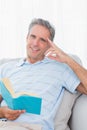 Man relaxing on his couch with a book smiling at camera Royalty Free Stock Photo