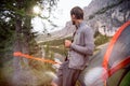 Man relaxing near hanging tent camping with hot beverage looking at lake panorama.Group of friends people summer Royalty Free Stock Photo