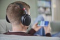 Rear View Of Man Relaxing On Sofa Wearing Wireless Headphones Streaming Film Music Or Podcast From Mobile Phone Royalty Free Stock Photo