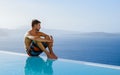 man relaxing in swimming pool during vacation at Santorini infinity looking out over the ocean