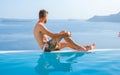 man relaxing in swimming pool during vacation at Santorini infinity looking out over the ocean