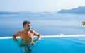 man relaxing in swimming pool during vacation at Santorini infinity looking out over the ocean Royalty Free Stock Photo