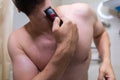 A man removes hair from his beard with an electric shaver. A man with an athletic figure in the bathroom