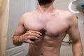 A man removes unwanted hair from his body using an electric razor. A man with an athletic figure in the bathroom