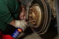 A man is repairing a car in a garage. A man treats rusted bolts with WD-40 solution. Replacing a brake disc on a car in