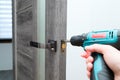Handyman Fitting A New Door Using A Screwdriver At Home. Carpenter at lock installation with electric drill into interior wood