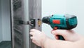 Handyman Fitting A New Door Using A Screwdriver At Home. Carpenter at lock installation with electric drill into interior wood