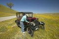 A man repairing his maroon Model T, surrounded by spring flowers off of Route 58, Shell Road, CA
